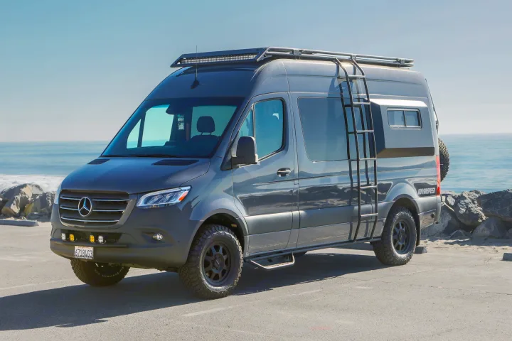 Adventure-ready dark gray Mercedes Sprinter **RV rental** camper van with off-road gear, parked by the ocean.. Mercedes Sprinter 2021