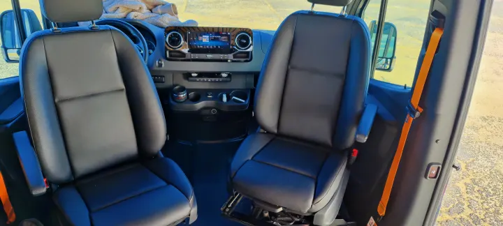 Spacious RV rental interior: black leather front seats and modern dashboard with an infotainment system, ready for your adventure.. Mercedes Sprinter 2021
