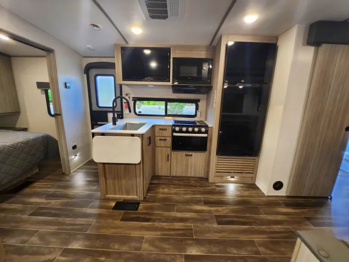 Explore this RV rental's modern interior: full kitchen, entertainment center, fridge, and cozy bedroom entry.. Keystone RV Passport GT Ultra Lite 2023