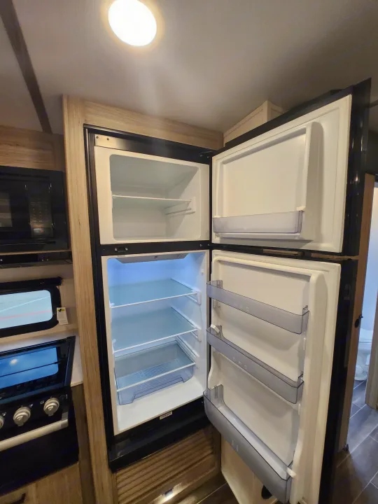 Ready for your RV rental adventure! View of a clean, open refrigerator and freezer within a well-equipped camper kitchen.. Keystone RV Passport GT Ultra Lite 2023