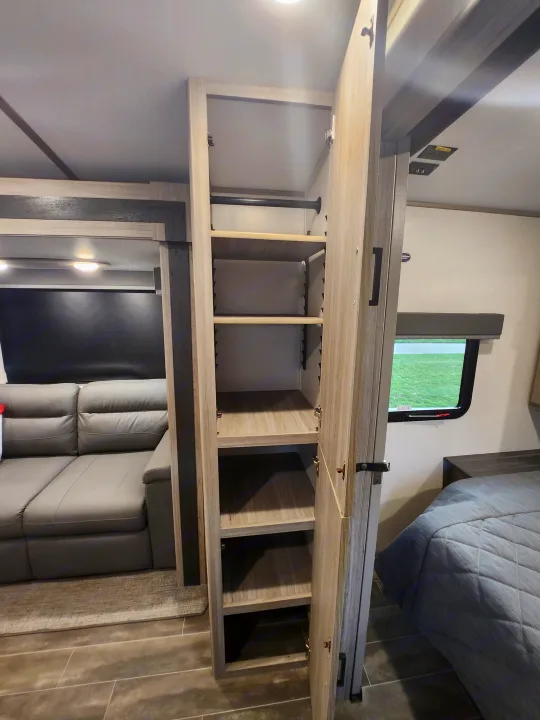 Explore this RV rental's versatile storage with an open closet, comfortable sofa, and a glimpse of the bedroom.. Keystone RV Passport GT Ultra Lite 2023