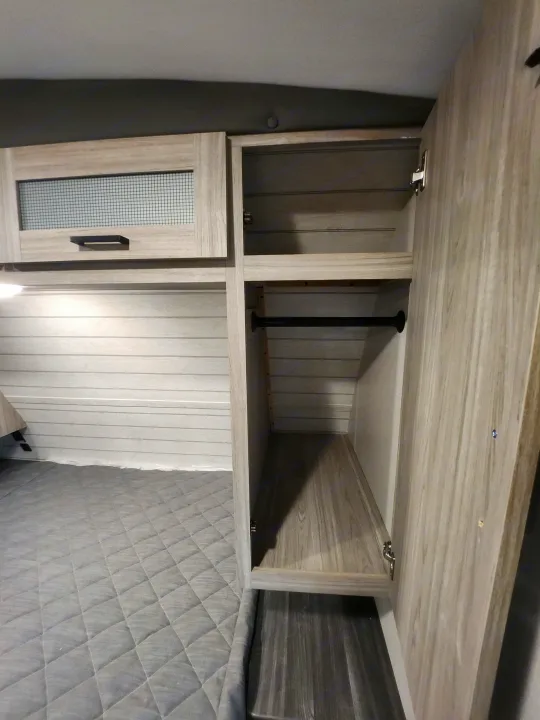 RV rental bedroom interior shows a bed, light wood shiplap wall, and open wardrobe with hanging bar.. Keystone RV Passport GT Ultra Lite 2023