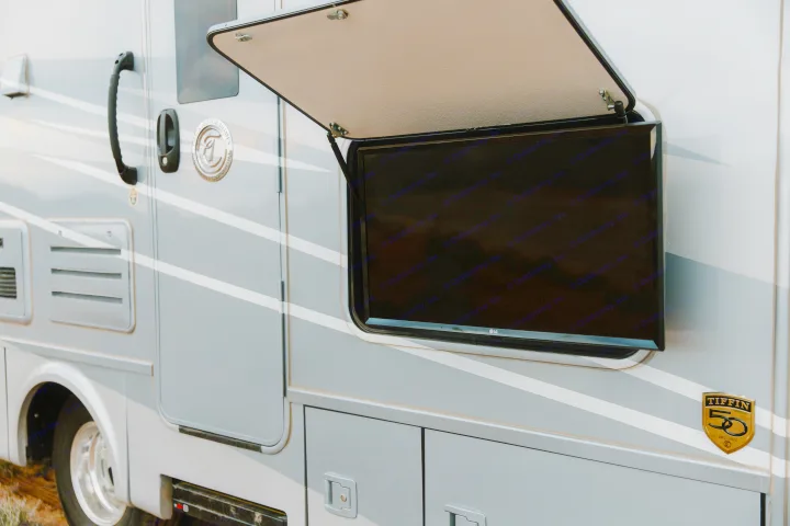 Side of a grey RV rental with an open outdoor LG TV compartment and Tiffin 50th-anniversary emblem.. Tiffin Motorhomes Wayfarer 25 JW 2021