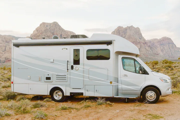 Experience nature with this sleek RV rental. A modern motorhome parked on rocky desert terrain, backed by majestic mountains.. Tiffin Motorhomes Wayfarer 25 JW 2021