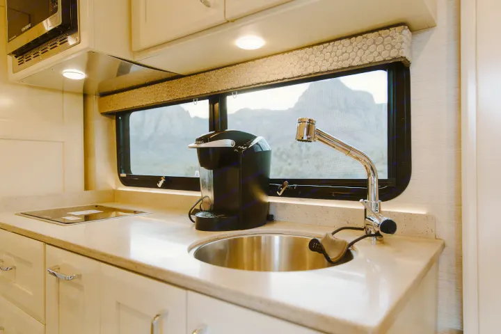 Modern RV rental kitchen featuring a sleek sink, Keurig coffee maker, cooktop, and a stunning mountain view out the window.. Tiffin Motorhomes Wayfarer 25 JW 2021