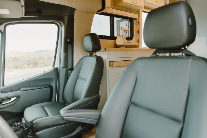 Inside this modern RV rental, see black front seats, a bright kitchen area, and a desert landscape through the window.. Tiffin Motorhomes Wayfarer 25 JW 2021