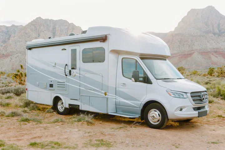A gray Tiffin Wayfarer RV rental, built on a Mercedes-Benz chassis, parked on a dirt road with mountains in a desert.. Tiffin Motorhomes Wayfarer 25 JW 2021