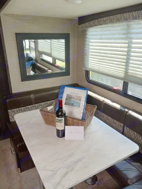 Welcoming RV rental dinette setup: a welcome basket with Fogg Winery wine, 'Bay Breeze' info binder, and comfy bench seating.. Dutchmen Kodiak Ultra Lite 2019