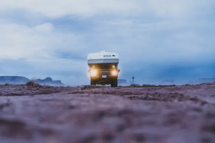 A Kodiak RV rental with bright headlights on, parked at dusk in a vast desert landscape with distant mountains and a windmill.. Ford Other 1996