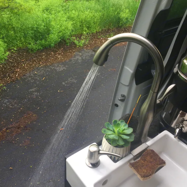 Compact RV rental sink setup: running water, succulent, and sponge by the vehicle door, perfect for outdoor use.. Freightliner Sprinter 2016