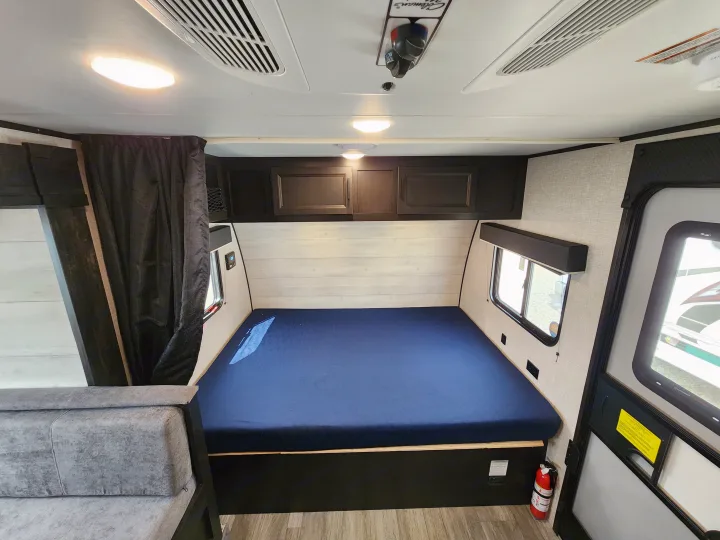 RV rental interior view: a comfortable blue bed, overhead cabinets, windows, and seating area. Great for travel.. Jayco slx 2023