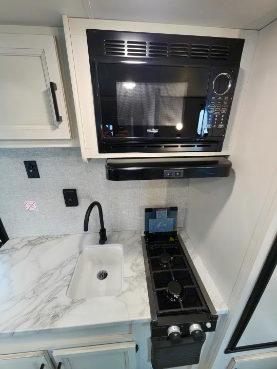 RV rental kitchen: a compact space with a microwave, two-burner stove, and sink, ready for convenient meal prep.. Jayco slx 2023