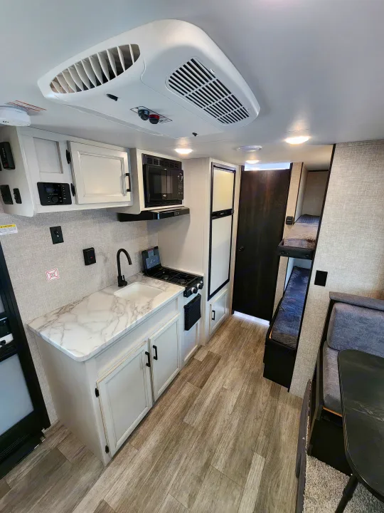 Bright rv rental interior featuring a functional kitchen with microwave, stove, & sink, plus flexible seating/bunk beds.. Jayco slx 2023