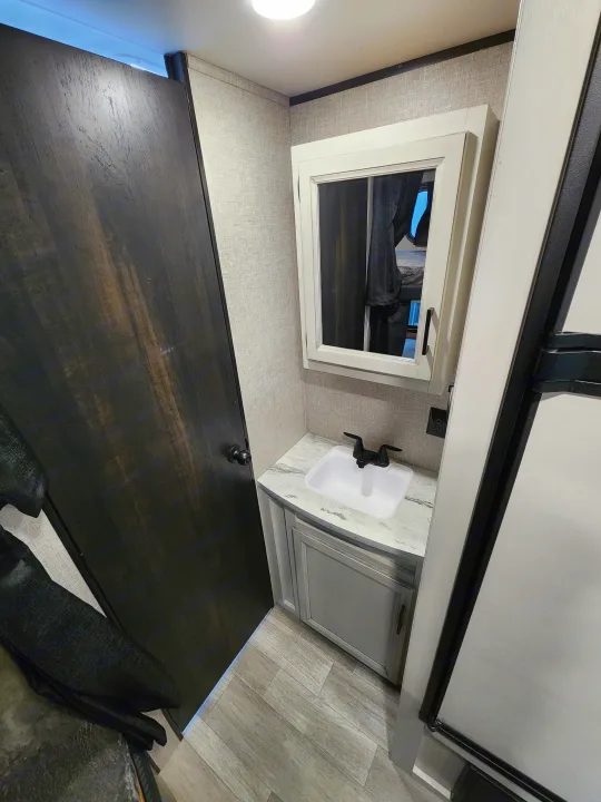Inside this RV rental: A stylish vanity area with a white sink, mirror reflecting a bed, dark wood counter, and light textured walls.. Jayco Jay Flight 2023