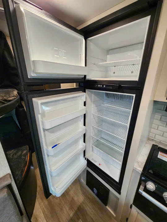 RV rental kitchen: Open refrigerator and freezer with wire shelves, door bins, and compact appliances.. Jayco Jay Flight 2023