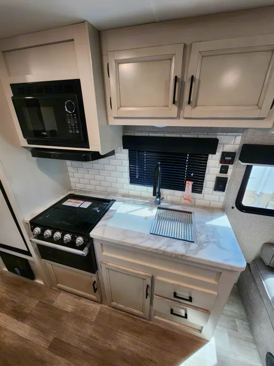 Top-down view of a modern RV rental kitchen: light cabinets, marble counter, built-in microwave, and oven.. Jayco Jay Flight 2023