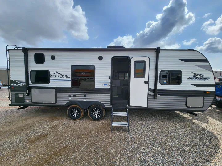 A modern white and gray Jayco Jay Flight SLX travel trailer, ideal for your next rv rental adventure, parked on a gravel lot.. Jayco Jay Flight 2023