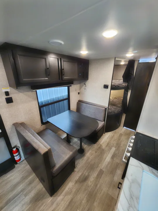 Spacious RV rental interior showcasing a cozy dinette with a table, kitchen area, bunk beds, and warm wood-look flooring.. Jayco Jay Flight 2023