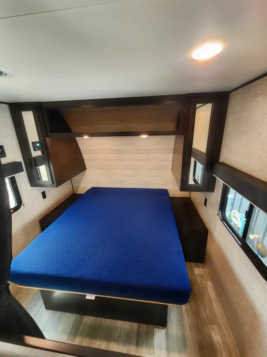 Inside an RV rental: a modern bedroom featuring a comfortable blue mattress, ample storage, and natural light from a skylight.. Jayco Jay Flight 2023