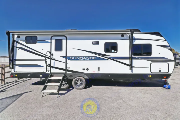 White Sundance Ultra Lite RV rental travel trailer with black accents, steps, and awning, parked on a gravel lot.. Heartland RVs Sundance Ultra Lite 2022