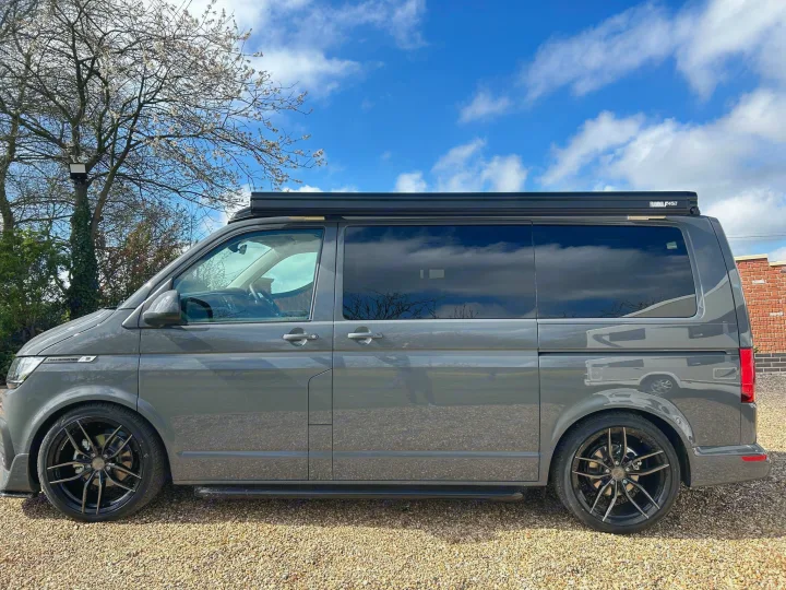 A sleek gray VW campervan, perfect for an RV rental. It has dark tinted windows, custom wheels & a Fiamma awning.. Volkswagen Other 2023