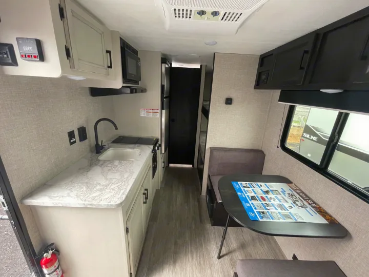 This RV rental's modern interior showcases a kitchen with sink, microwave, and stovetop, alongside a cozy dinette area.. Jayco Jay Flight 2023