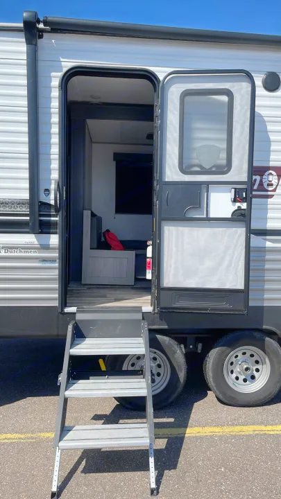 RV rental: A travel trailer with its main door and screen door open, revealing the interior steps extended to the ground.. Coleman Lantern 242BH 2022