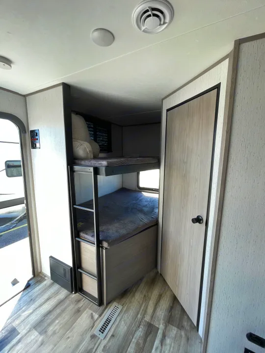 Cozy bunk beds and modern light wood interior in this inviting rv rental, featuring a ceiling vent and wall control panel.. Coleman Lantern 242BH 2022