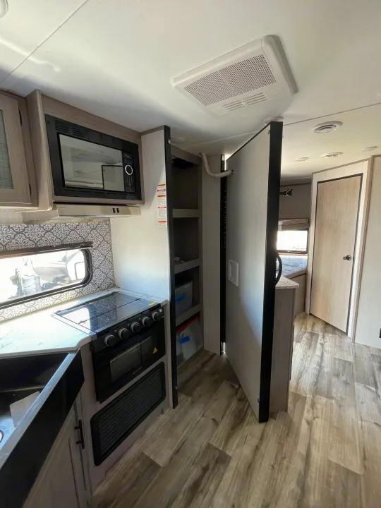 Spacious RV rental kitchen featuring modern appliances like a microwave and stove, plus clever pantry storage.. Coleman Lantern 242BH 2022