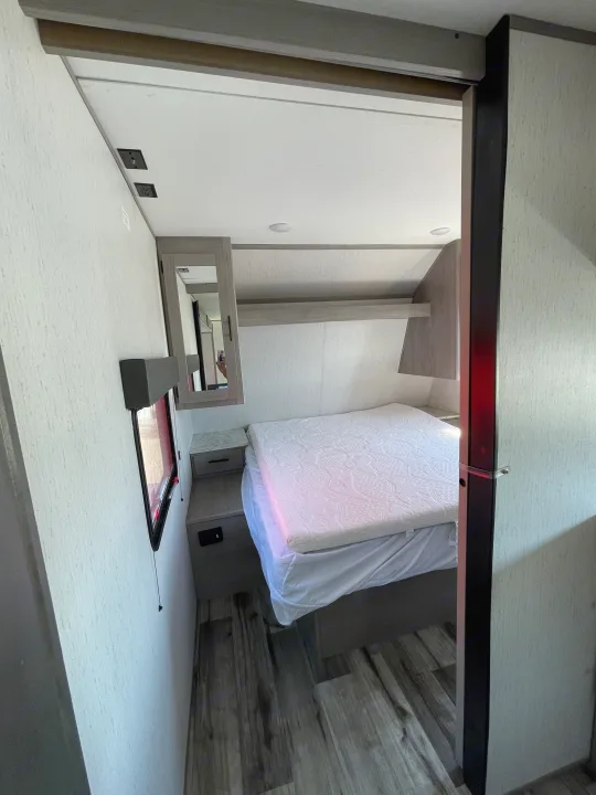 Modern RV rental bedroom featuring a neat bed, built-in storage, power outlets, and wood-look flooring.. Coleman Lantern 242BH 2022