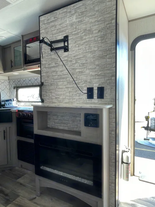 Modern rv rental interior: Faux brick accent wall with TV mount, built-in entertainment system, electric fireplace, and kitchen amenities.. Coleman Lantern 242BH 2022
