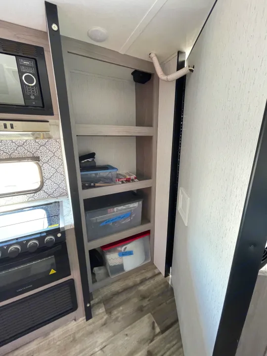 RV rental kitchen: microwave, oven, built-in shelving with storage bins, and a patterned backsplash.. Coleman Lantern 242BH 2022
