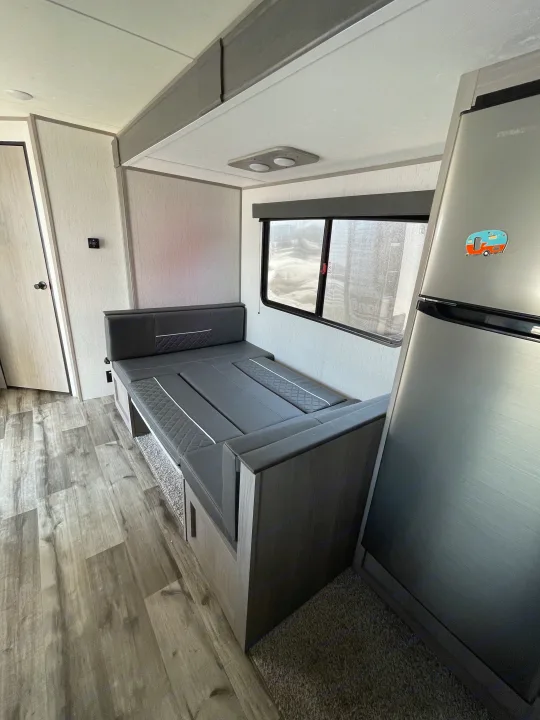 Spacious interior of an RV rental featuring a dark grey dinette, large fridge, and wood-look flooring.. Coleman Lantern 242BH 2022