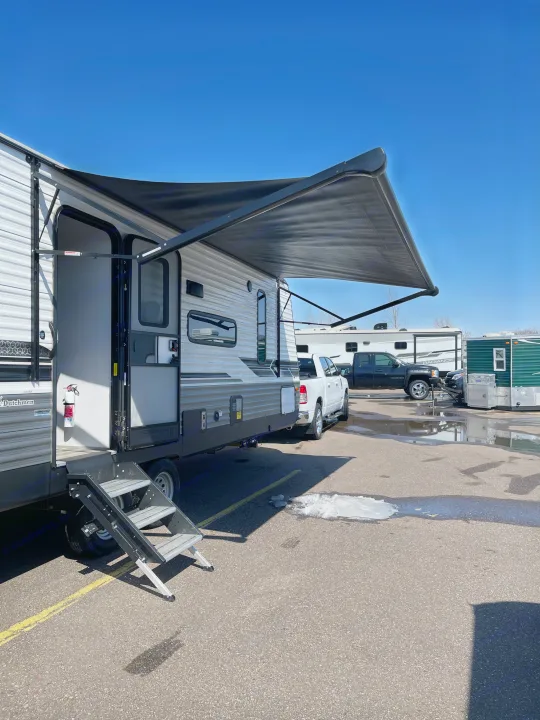 Light-colored RV rental with its black awning extended, parked on asphalt, steps lowered. Perfect for outdoor escapes.. Coleman Lantern 242BH 2022