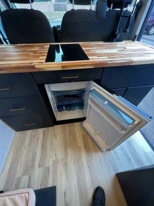 Explore this RV rental's modern kitchen: wood counter, induction cooktop, sink, and accessible built-in fridge. Dodge Ram Promaster 2500 2022