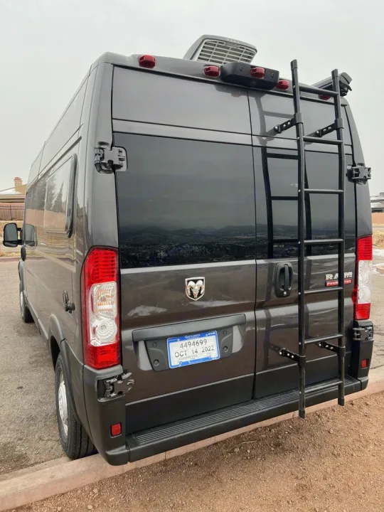 Rear view of a dark gray Ram ProMaster camper van RV rental, featuring a rear ladder and roof AC unit.. Dodge Ram Promaster 2500 2022