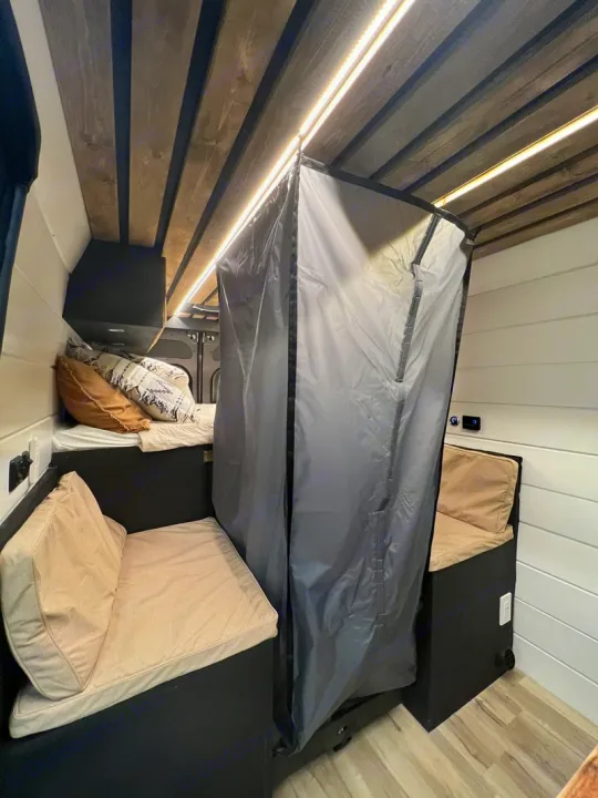 Cozy RV rental interior with bed, seating, portable gray shower, wood-slat ceiling, and warm LED lighting.. Dodge Ram Promaster 2500 2022