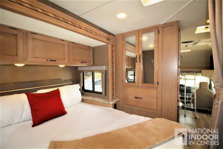 Inside an RV rental: cozy bedroom with light wood cabinets, red pillow on white bed, mirrored wardrobe & driver's area view.. Thor Motor Coach Freedom Elite 2018