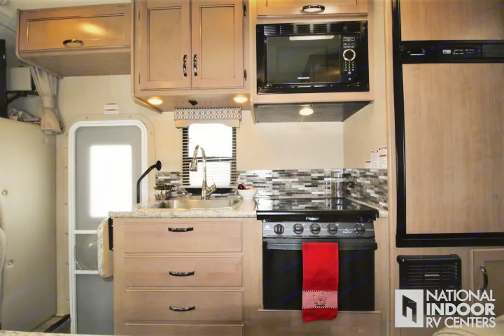 Inside an RV rental, this bright kitchen offers a microwave, stove, sink, and light wood cabinets, plus a fridge.. Thor Motor Coach Freedom Elite 2018