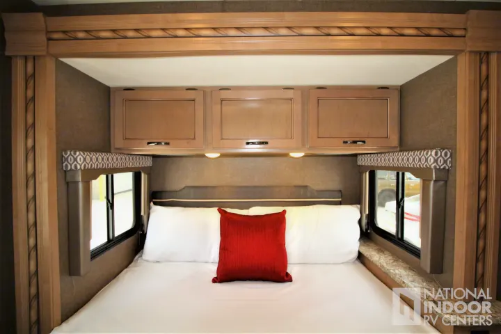 RV rental bedroom with a comfortable bed, white linens, red pillow, overhead cabinets, and windows for compact travel.. Thor Motor Coach Freedom Elite 2018