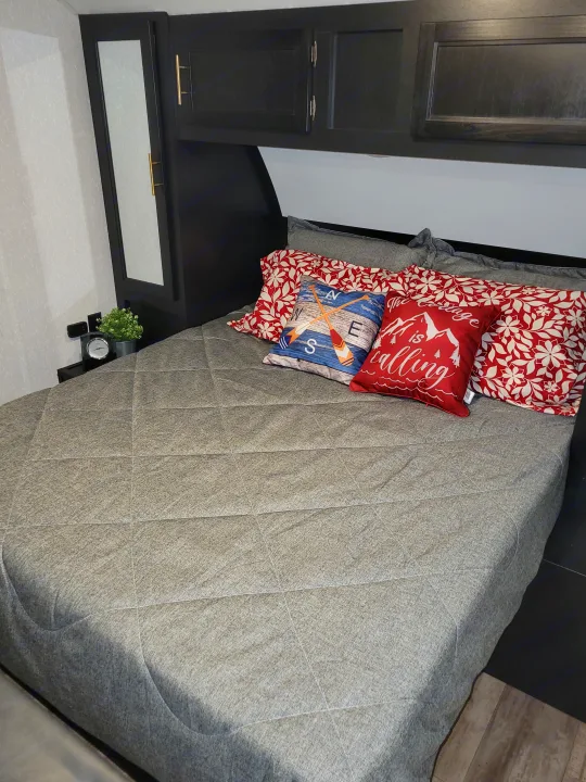 Cozy RV rental bedroom featuring a comfy bed with decorative pillows, compact storage, and a small nightstand.. Forest River Cherokee Grey Wolf 2022