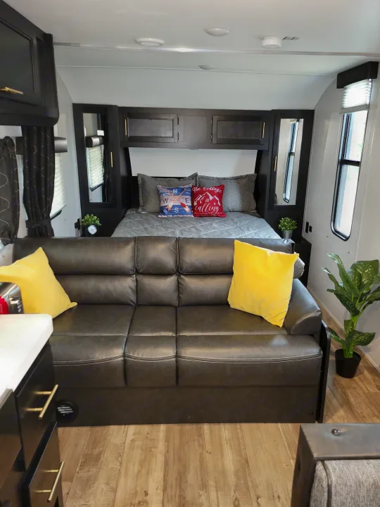 Tour this stylish rv rental: a cozy living space with a dark sofa, bright yellow pillows, and a welcoming bed.. Forest River Cherokee Grey Wolf 2022