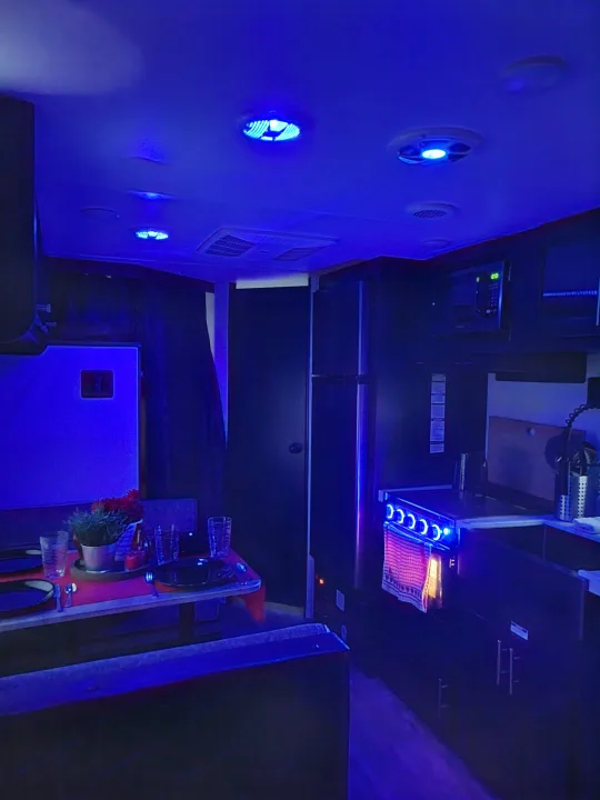 Modern rv rental interior, featuring a kitchen and dining area illuminated by unique blue ambient lighting.. Forest River Cherokee Grey Wolf 2022