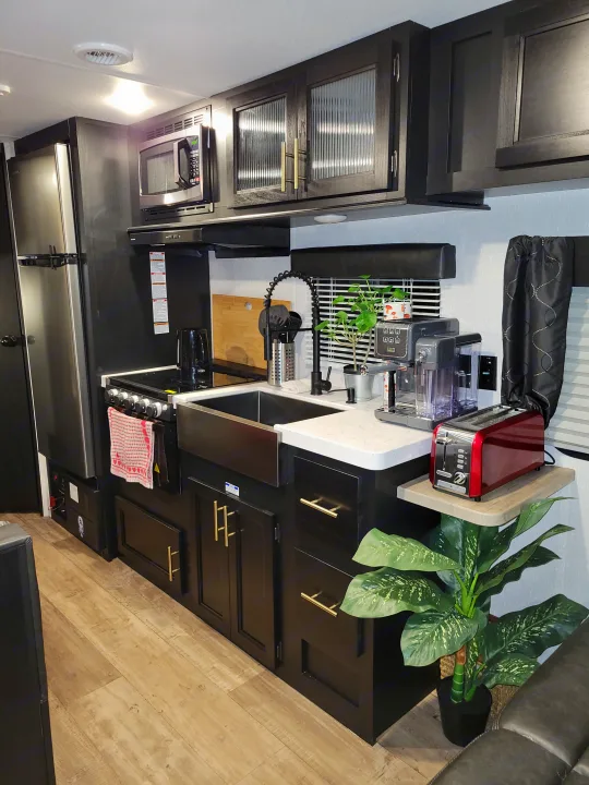 Modern RV rental kitchen with black cabinets, stainless steel appliances, and a farm sink, ready for travel.. Forest River Cherokee Grey Wolf 2022