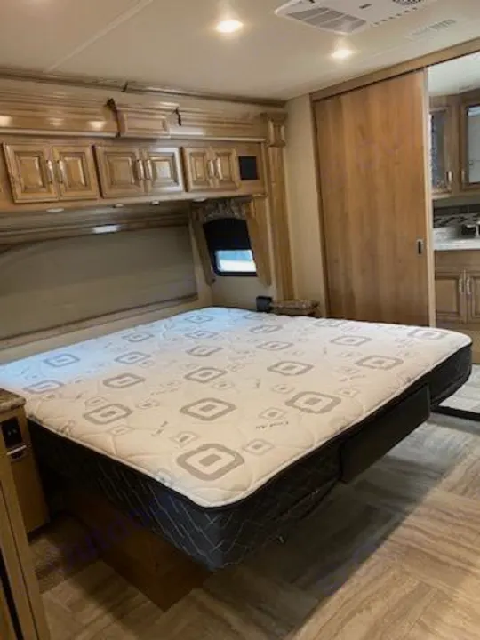 Spacious RV rental bedroom features a patterned mattress, overhead wood cabinets, and a sliding door.. Holiday Rambler Navigator 2019