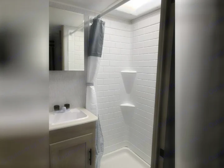 Modern RV rental bathroom featuring a white tile-look shower, sink, mirror, and vanity for comfortable travel.. Forest River Evo 2023