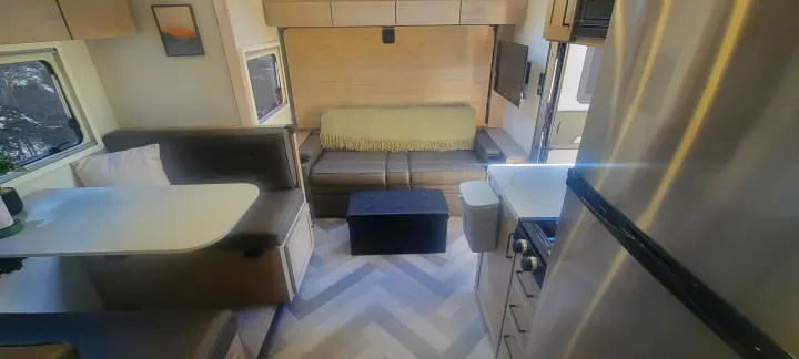 This RV rental's interior boasts a functional dinette, cozy sofa bed, and compact kitchen with modern appliances.. Ember Overland 2023