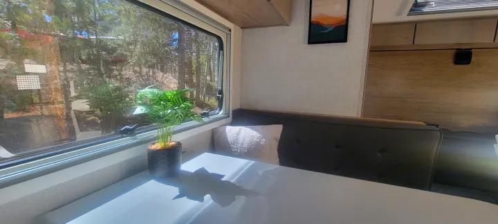 Inside a comfortable RV rental: dinette, forest views, and a cozy plant. Relax and enjoy nature's beauty.. Ember Overland 2023