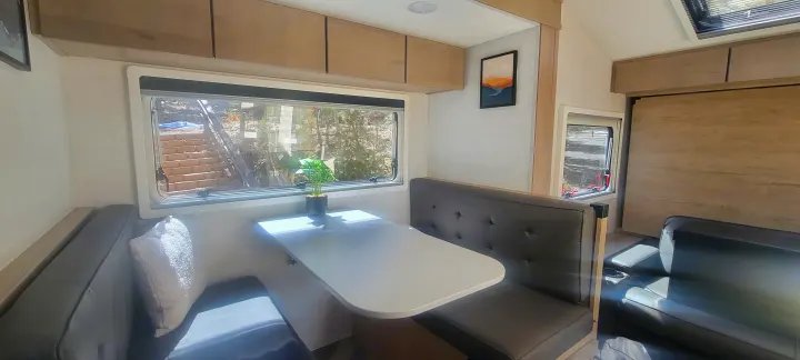 Inside this RV rental: a cozy dinette with window views, comfortable seating, and overhead storage. Ideal for travel.. Ember Overland 2023