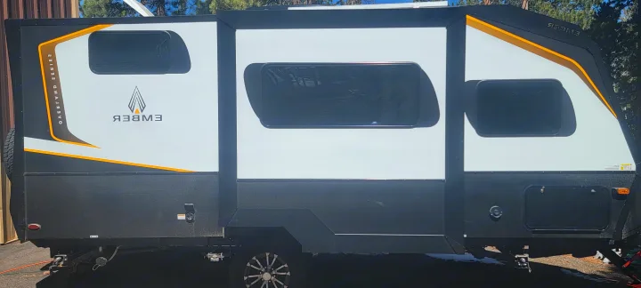 This modern Ember rv rental showcases a white and black exterior with orange accents and multiple windows, some on slide-outs.. Ember Overland 2023